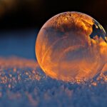 Close-up shot of a frozen bubble with warm reflections resting on a snowy surface at twilight.